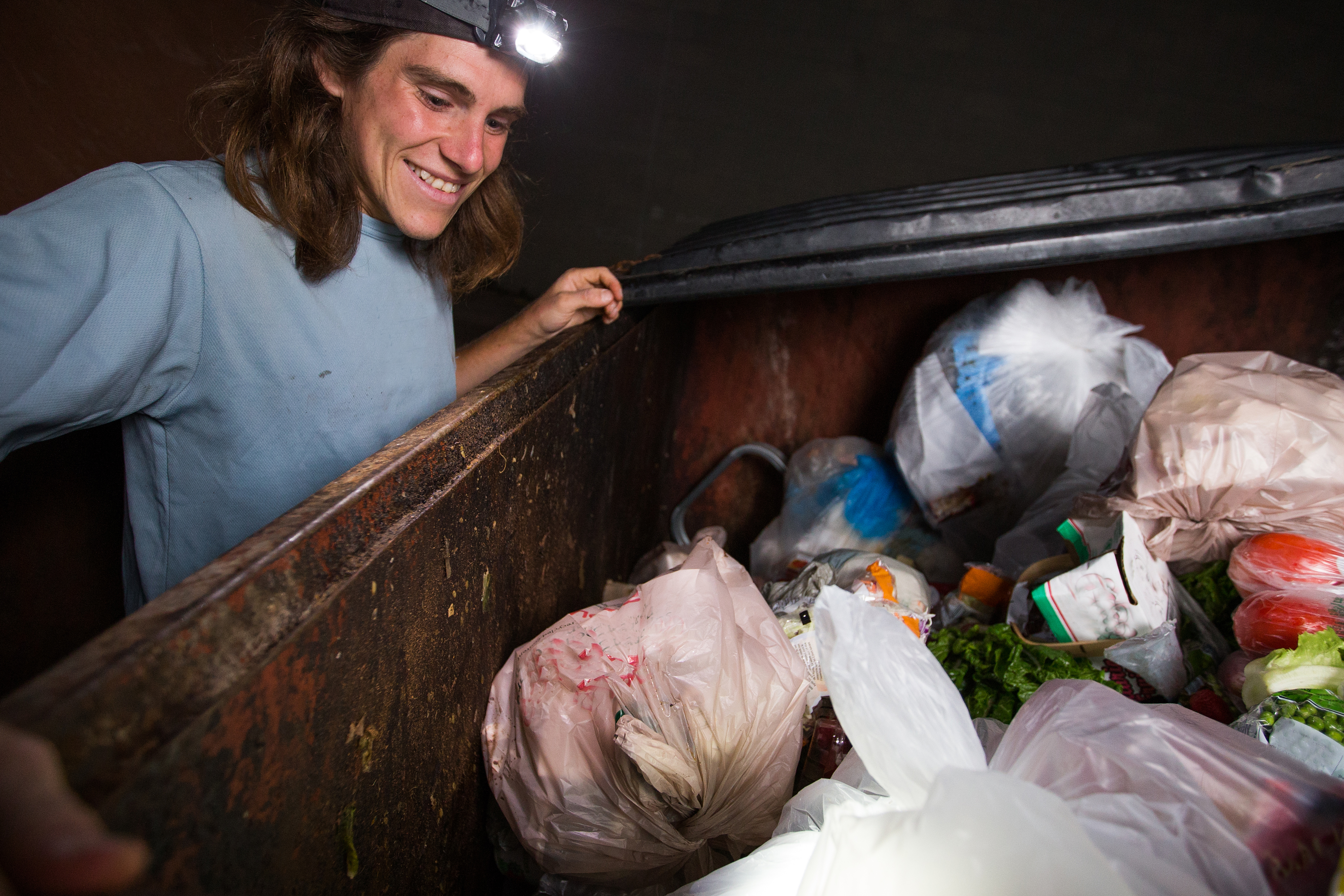 dumpster diving at night - smiling man looking into a dumpster